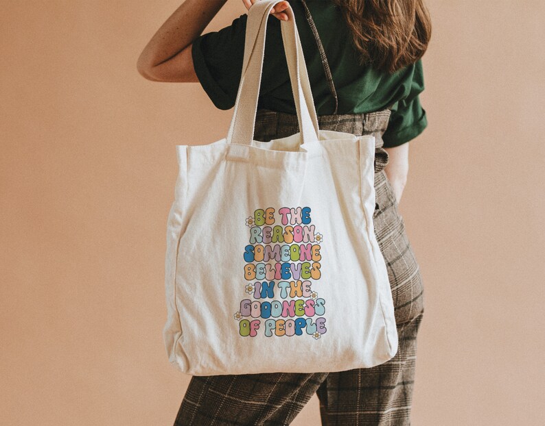 May include: A white tote bag with a colorful graphic that reads "Be the reason someone believes in the goodness of people".