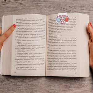 May include: A close-up of an open book with a pink and blue bookmark featuring the words "Book Besties". The book is open to a page with text in Spanish.