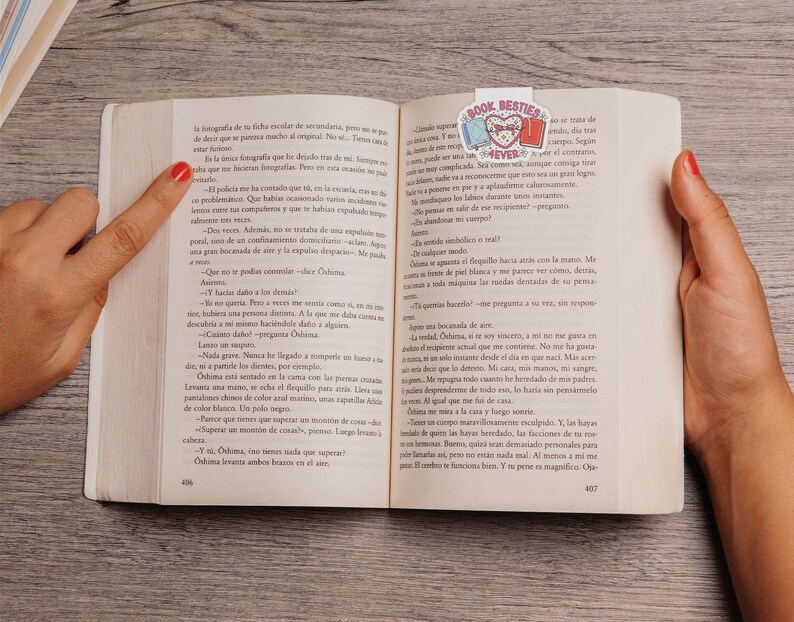 May include: A close-up of an open book with a pink and blue bookmark featuring the words "Book Besties". The book is open to a page with text in Spanish.