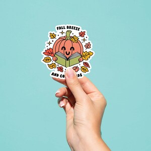 May include: A sticker with a cartoon pumpkin reading a book. The sticker says "Fall Breeze and Cozy Reads".