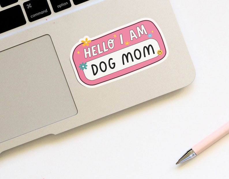 Peut inclure: Autocollant rose avec le texte "Hello I am Dog Mom" en lettres blanches. L'autocollant a une bordure blanche et est d&eacute;cor&eacute; de petites fleurs et d'&eacute;toiles.
