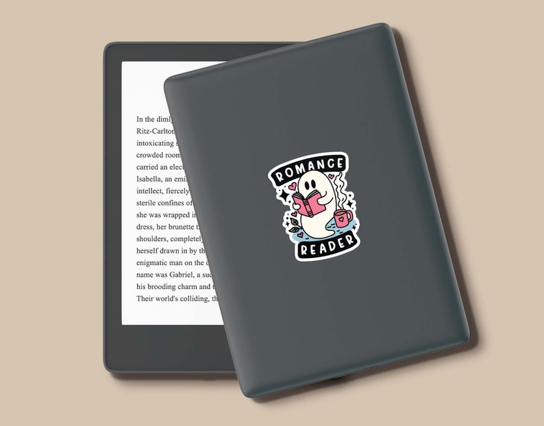 Op de afbeelding: Een zwarte en grijze e-reader met een sticker van een geest die een boek leest en een kopje koffie vasthoudt. De sticker zegt "Romance Reader".