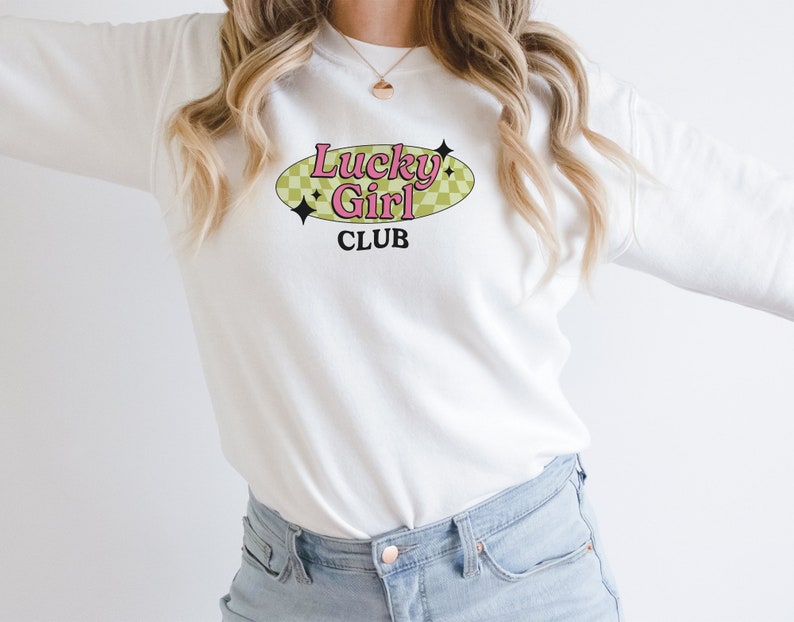 May include: White sweatshirt with a pink and green graphic that says "Lucky Girl Club" in a retro style.