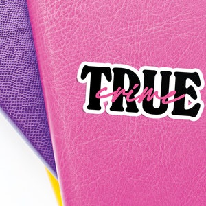 May include: A pink leather notebook with a black and white sticker that says "TRUE crime" in pink lettering.