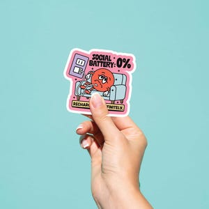 May include: A sticker featuring a cartoon illustration of a red character with a sad expression, lounging on a small blue couch. The sticker reads "Social Battery: 0%" and "Recharge Definitely."