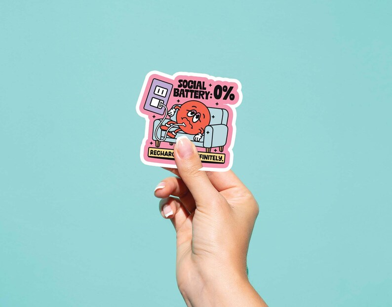 May include: A sticker featuring a cartoon illustration of a red character with a sad expression, lounging on a small blue couch. The sticker reads "Social Battery: 0%" and "Recharge Definitely."
