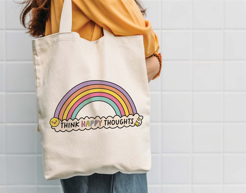 May include: A white canvas tote bag with a rainbow and the text "Think Happy Thoughts" in colorful letters. The rainbow has a yellow smiley face at the bottom left and a yellow star at the bottom right.