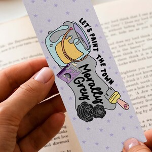 May include: A bookmark with a purple, gray, and yellow paint can design. The text on the bookmark reads "Let's paint the town morally grey".