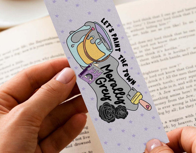 May include: A bookmark with a purple, gray, and yellow paint can design. The text on the bookmark reads "Let's paint the town morally grey".