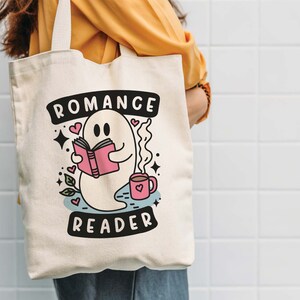 Op de afbeelding: Een witte canvas tote bag met een geest die een boek leest en een kopje koffie vasthoudt. De tekst op de tas is "Romance Reader".