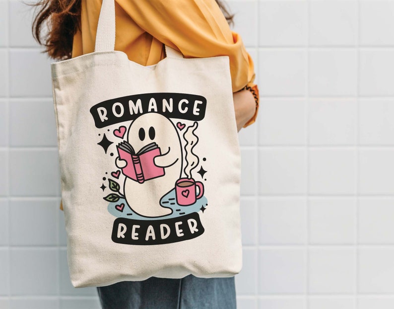 Op de afbeelding: Een witte canvas tote bag met een geest die een boek leest en een kopje koffie vasthoudt. De tekst op de tas is "Romance Reader".