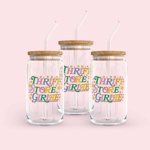 May include: A white ceramic mug with a black handle and the text "But First, Coffee" in a bold, black font. The mug is sitting on a wooden surface. The mug is 4 inches tall.