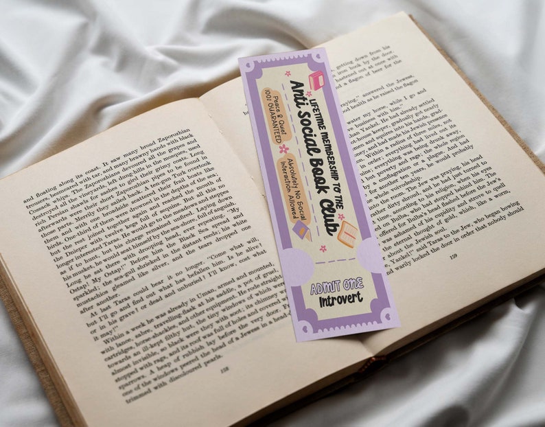 Puede incluir: Un marcap&aacute;ginas morado y blanco con el texto "LIFETIME MEMBERSHIP TO THE ANTI SOCIAL BOOK CLUB" y "ADMIT ONE Introvert". El marcap&aacute;ginas presenta una ilustraci&oacute;n de dibujos animados de un libro con una taza de t&eacute; y una porci&oacute;n de pastel.