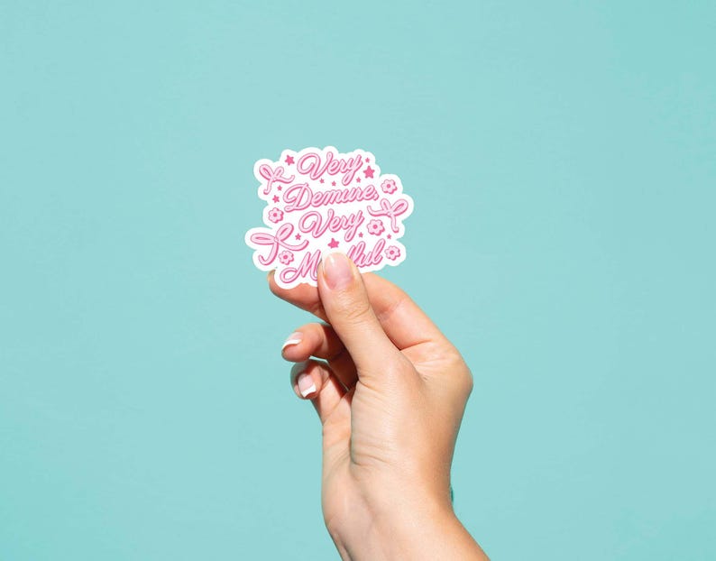 May include: A white sticker with pink lettering that reads "Very Demine, Very Much!" with pink flower accents.