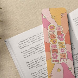 K&ouml;nnte beinhalten: Ein rosa und orangefarbenes Lesezeichen mit einem wellenf&ouml;rmigen Design und dem Text "One More Chapter!" in einer Retro-Schrift.
