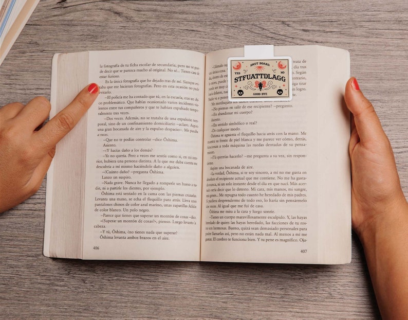Puede incluir: Primer plano de un libro con un marcap&aacute;ginas que presenta una ouija blanca y marr&oacute;n con el texto "STFUATTDLAGG" y "GOOD BYE".