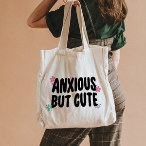 May include: A white canvas tote bag with black text that reads "anxious but cute" and colourful flower accents.