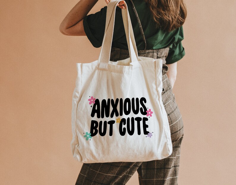 May include: A white canvas tote bag with black text that reads "anxious but cute" and colourful flower accents.