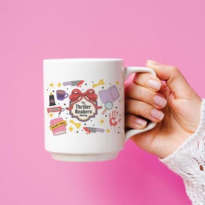 May include: White ceramic mug featuring the text "The Thriller Readers Society" with illustrations of a knife, book, magnifying glass, and other thriller-themed icons. The mug is held against a pink background.