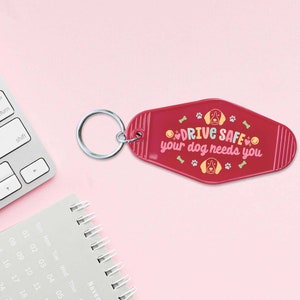 May include: Red keychain with a white and pink "DRIVE SAFE your dog needs you" message and a cartoon dog illustration.