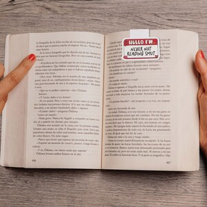 May include: A close-up of a book with a bookmark that reads "Hello I'm Never Not Reading Smut". The bookmark is white with red and black text. The book is open to a page with Spanish text.