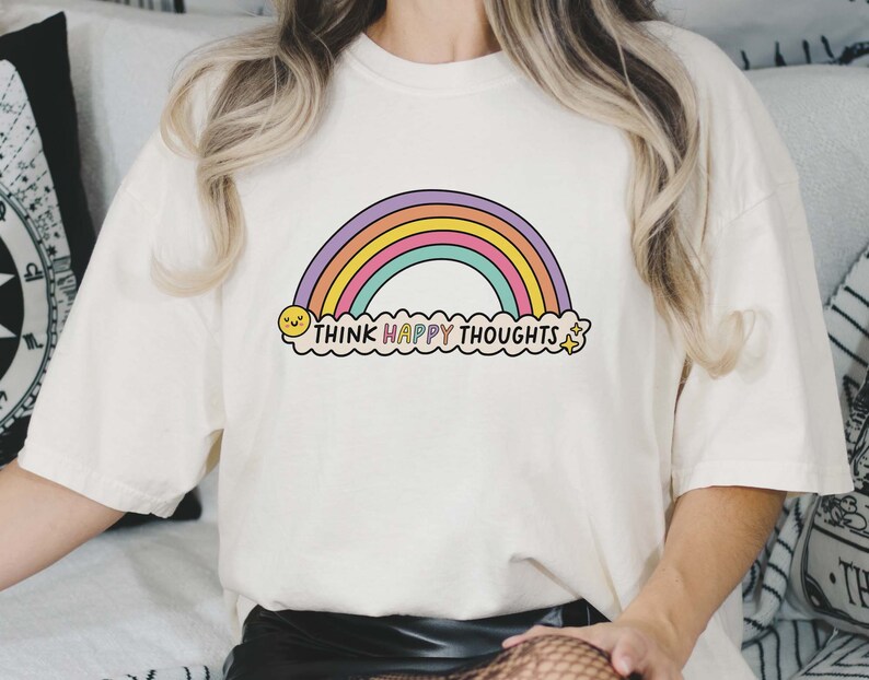 May include: White t-shirt with a rainbow and the text "Think Happy Thoughts" printed on it.