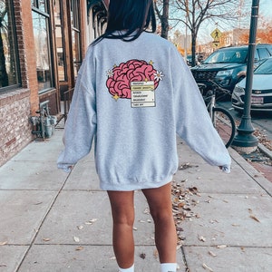 May include: Grey sweatshirt with a pink brain graphic and a text box that says "Properties: Manage Anxiety,  Self-Esteem, Boundaries,  Thoughtful,  Remarkable,  Turn Out".