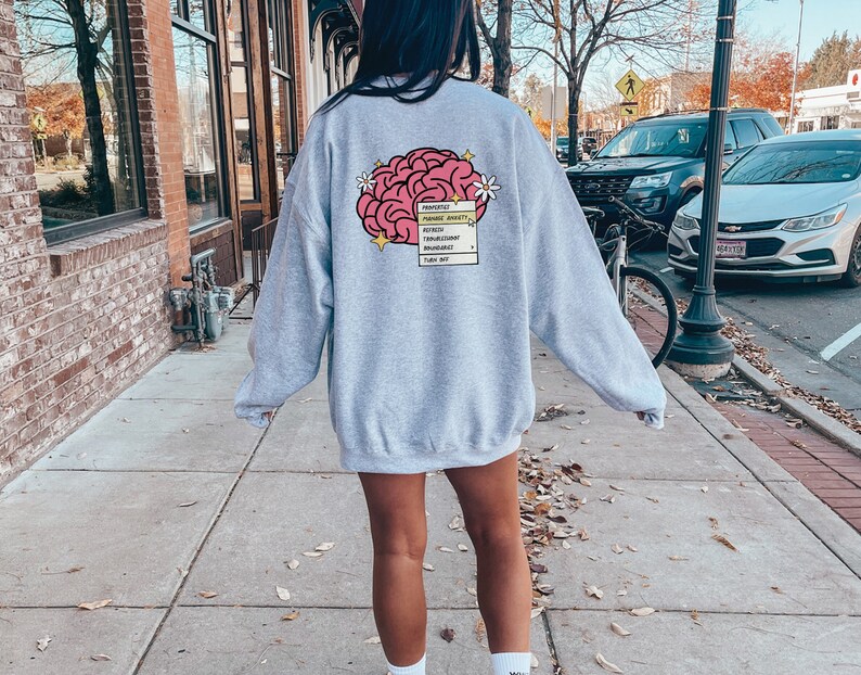 May include: Grey sweatshirt with a pink brain graphic and a text box that says "Properties: Manage Anxiety,  Self-Esteem, Boundaries,  Thoughtful,  Remarkable,  Turn Out".