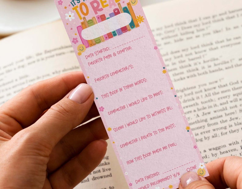 May include: Pink bookmark with a floral design and the text "It's Time To Read". The bookmark has a checklist for tracking reading progress, including sections for date started, favorite page and chapter, favorite character, this book in three words, character I would like to meet, scene I would like to witness IRL, character I relate to the most, how this book made me feel, date finished, and would recommend? Y/N.