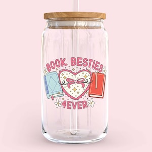 May include: A clear glass reusable water bottle with a wooden lid and a straw. The bottle has a pink and white sticker with the text "Book Besties 4ever" and a heart with two books inside.