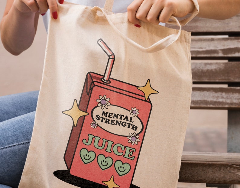 Puede incluir: Una bolsa de lona blanca con un dise&ntilde;o de caja de jugo de dibujos animados rosa y roja. La caja de jugo dice "Mental Strength Juice" y tiene tres corazones sonrientes en ella. Tambi&eacute;n hay estrellas brillantes y una pajita que sale de la parte superior.