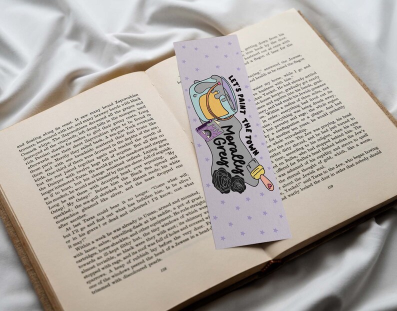 May include: A purple and white bookmark with a paint can, paintbrush, and flowers. The text on the bookmark reads "Let's paint the town Morally Grey".