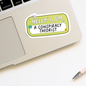 May include: A yellow sticker with rounded corners and a white border. The sticker says "Hello I am a conspiracy theorist" with a smiley face in the corner.