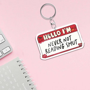 May include: White keychain with a red name tag that says "Hello I'm Never Not Reading Smut". The name tag has a red flame and two cherries on it.