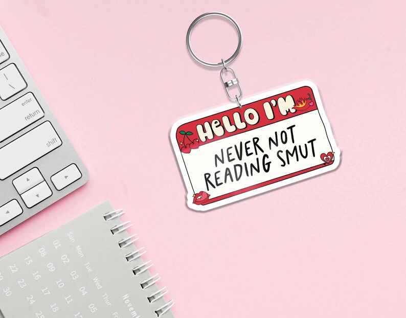 May include: White keychain with a red name tag that says "Hello I'm Never Not Reading Smut". The name tag has a red flame and two cherries on it.