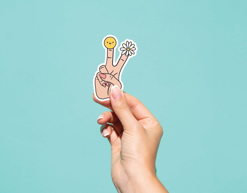 May include: A sticker of a hand making the peace sign with a smiley face on one finger and a daisy on the other finger.