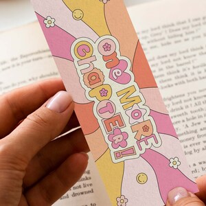 K&ouml;nnte beinhalten: Ein rosa und gelbes Lesezeichen im Retro-Design. Das Lesezeichen hat ein wellenf&ouml;rmiges Muster in rosa, gelber und wei&szlig;er Farbgebung. Der Text "One More Chapter!" ist in fetter, wei&szlig;er Schrift geschrieben.