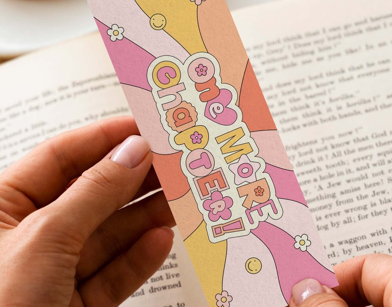 K&ouml;nnte beinhalten: Ein rosa und gelbes Lesezeichen im Retro-Design. Das Lesezeichen hat ein wellenf&ouml;rmiges Muster in rosa, gelber und wei&szlig;er Farbgebung. Der Text "One More Chapter!" ist in fetter, wei&szlig;er Schrift geschrieben.