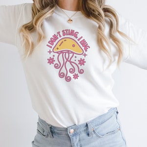 K&ouml;nnte beinhalten: Wei&szlig;er Pullover mit einem rosa und gelben Quallen-Motiv und dem Text "I don't sting I hug".