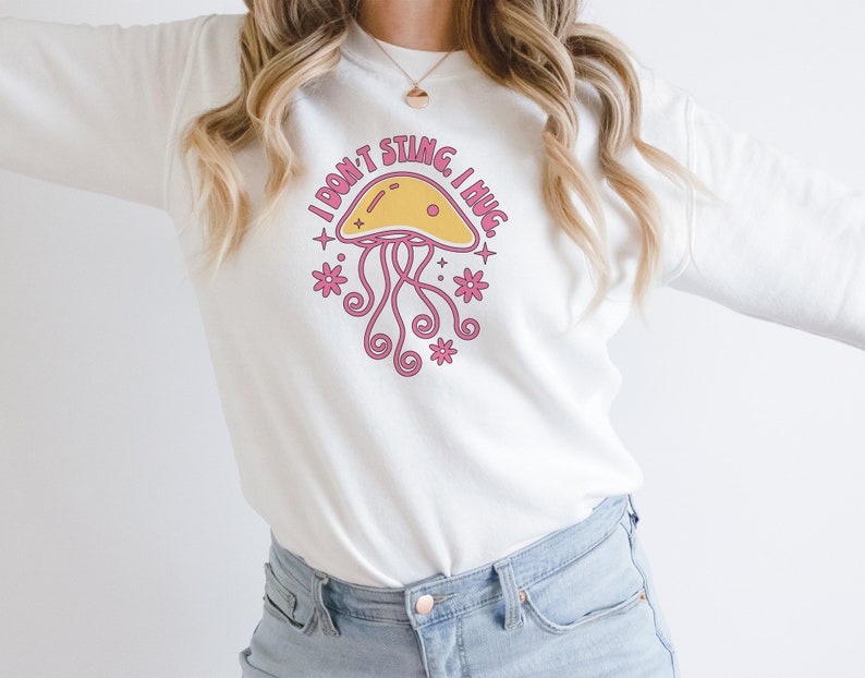 K&ouml;nnte beinhalten: Wei&szlig;er Pullover mit einem rosa und gelben Quallen-Motiv und dem Text "I don't sting I hug".