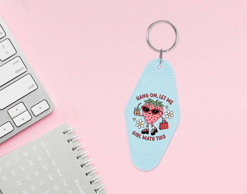 May include: A light blue key chain shaped like a motel key with a cartoon strawberry wearing sunglasses and holding a drink and a purse. The text on the key chain reads "Hang on, let me girl math this".