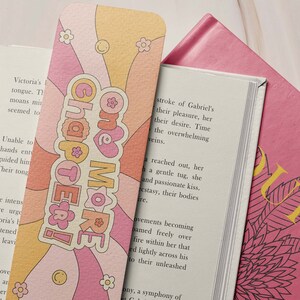 K&ouml;nnte beinhalten: Ein rosa und orangefarbenes Lesezeichen mit Retro-Design. Das Lesezeichen zeigt den Text "Chapter One More" in wei&szlig;er Schrift mit einem rosa Herzen.