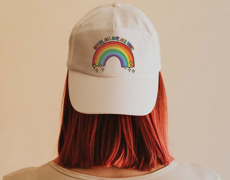 K&ouml;nnte beinhalten: Wei&szlig;e Baseballkappe mit einem Regenbogen und dem Text "Queer, All Day, All Year".