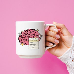 May include: White ceramic mug featuring a pink brain illustration and a yellow pop-up menu that reads "PROPERTIES: MANAGE ANXIETY, REFRESH, TROUBLESHOOT, BOUNDARIES, TURN OFF".