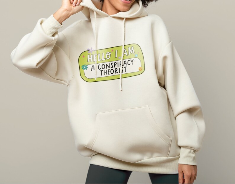May include: A cream-colored hoodie with a green name tag that says "Hello I am a conspiracy theorist" in a colorful font.