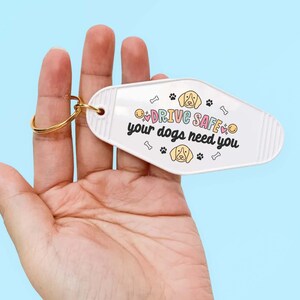 May include: White motel key chain with a gold ring. The keychain has a cartoon dog and the text "DRIVE SAFE your dogs need you".