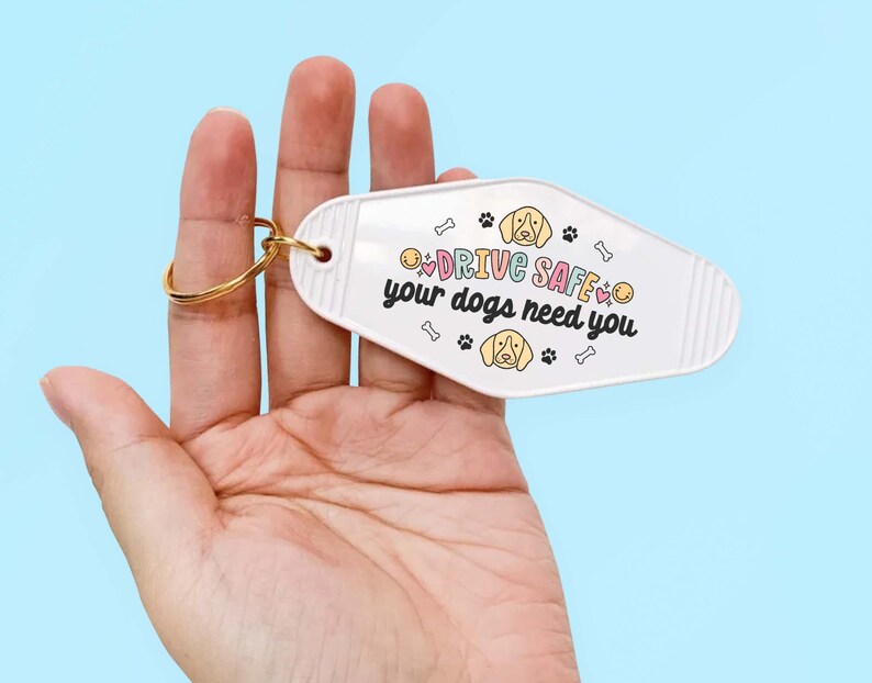May include: White motel key chain with a gold ring. The keychain has a cartoon dog and the text "DRIVE SAFE your dogs need you".