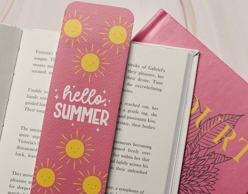 May include: Pink bookmark with yellow smiling suns and the words "hello SUMMER" in white. The bookmark is inserted into a book with white pages and a pink cover.