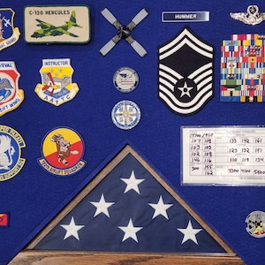 May include: A blue felt shadow box with a framed American flag, a variety of military patches, and a rank insignia. The text "HUMMER" is visible on the top of the shadow box.