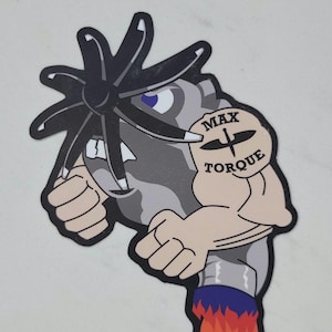 May include: A sticker featuring a cartoon character with a propeller head and muscular arms. The character has a gray body, blue eyes, and a tan arm with a tattoo that says "MAX TORQUE". The character's lower body has a blue and red flame design.